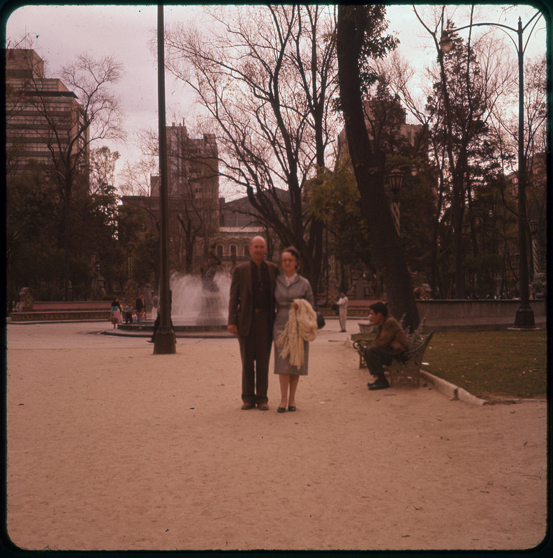 A photographic slide of Donald and Evelyn Crabtree standing together in front of a fountain in a city park. Photo is slightly blurry.