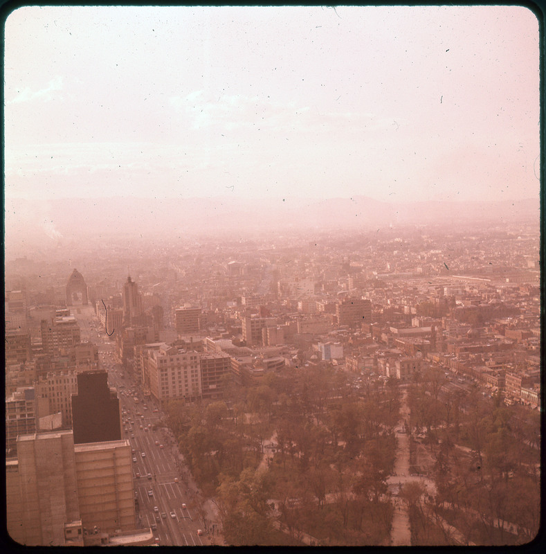 A photographic slide of a large city form an aerial view. There is a haze over the city.