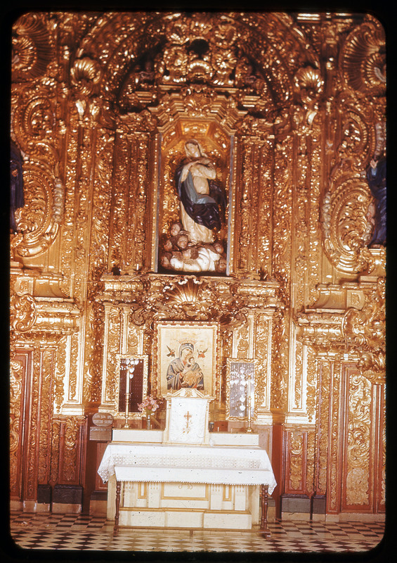 A photographic slide of a golden ornate interior to a church. There is an altar with a virgin mary painting and statue.