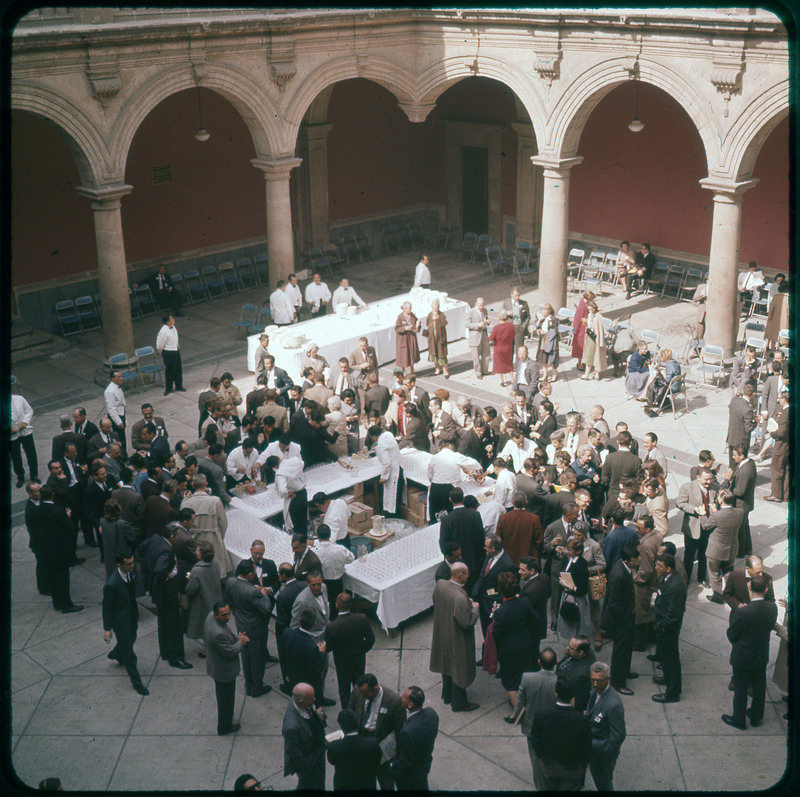 A photographic slide of many people at an event in a large room. The event is catered and some people are sitting.