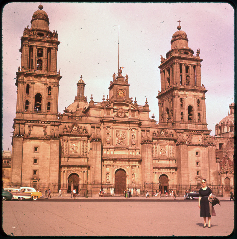 A photographic slide of Evelyn Crabtree posing in front of a large building called the Mexico City Metropolitan Cathedral. There are some people on the sidewalk out front of the building.