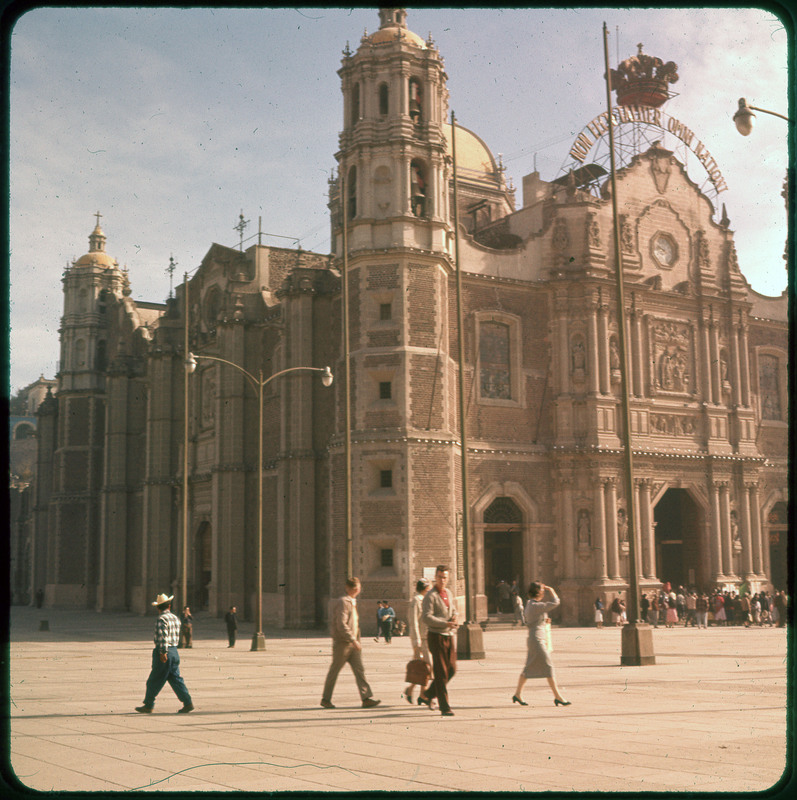 A photographic slide of Basilica of Our Lady of Guadalupe building. There are many people outside the building on the sidewalk.