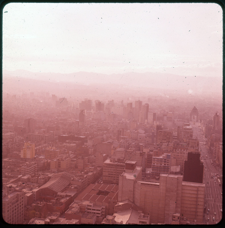 A photographic slide of a hazy city scape. There are mountains in the background and skyscrapers.