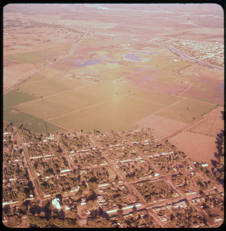 A photographic slide of many agricultural fields. There is a river, lakes, and a city in the background. There are neighborhoods in the foreground.