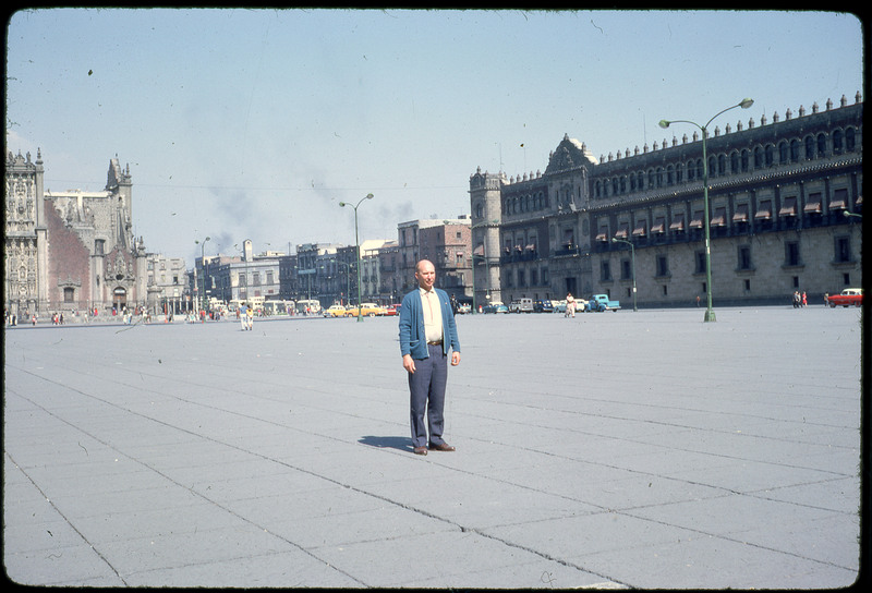 A photographic slide of Don E. Crabtree standing in a large urban area near a few historical buildings.