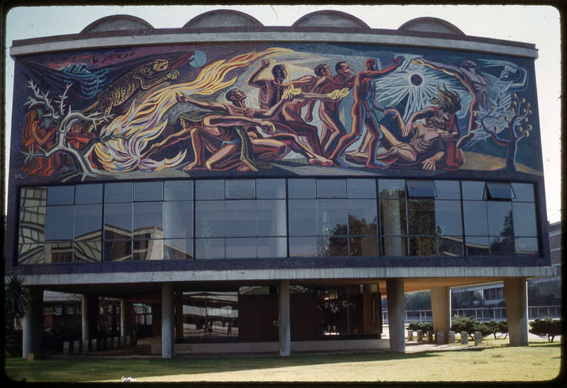 A photographic slide of a painting adorning the front of a building depicting an artistic rendition of the ancient history of mankind.