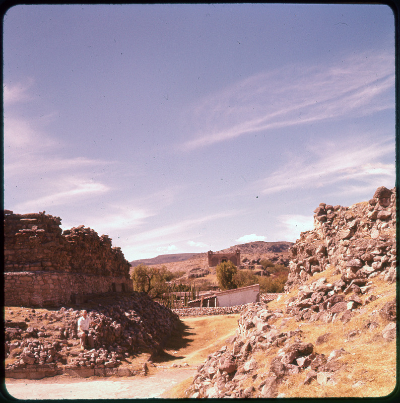 A photographic slide of rocky mountains and two buildings in the distance. They are large buildings with many cactuses surrounding.