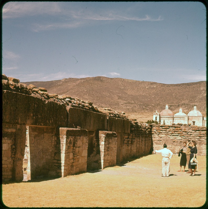 A photographic slide of stone walls with mountains and a building in the background.