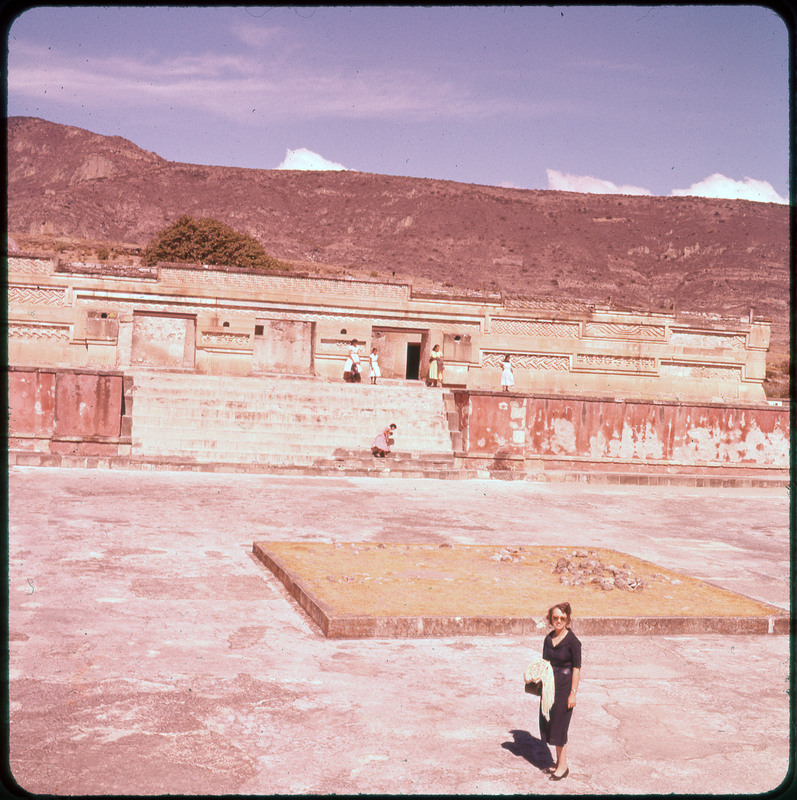 A photographic slide of Evelyn Crabtree posing in a stone courtyard. The walls have geometric carvings and there are mountains in the background.