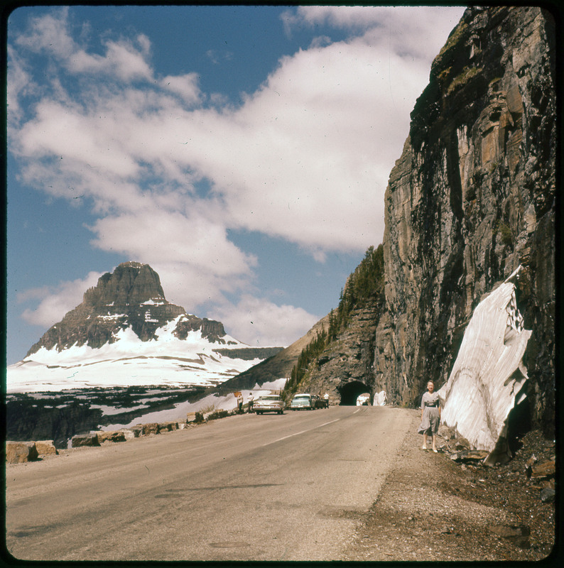 A photographic slide of Evelyn Crabtree standing on the side of the road. There are many large snowy mountains in the background.