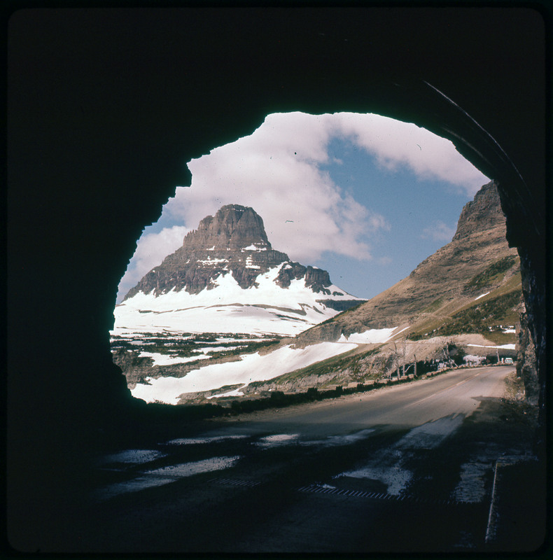 A photographic slide of a snowy mountain range. The photo is taken from a tunnel.