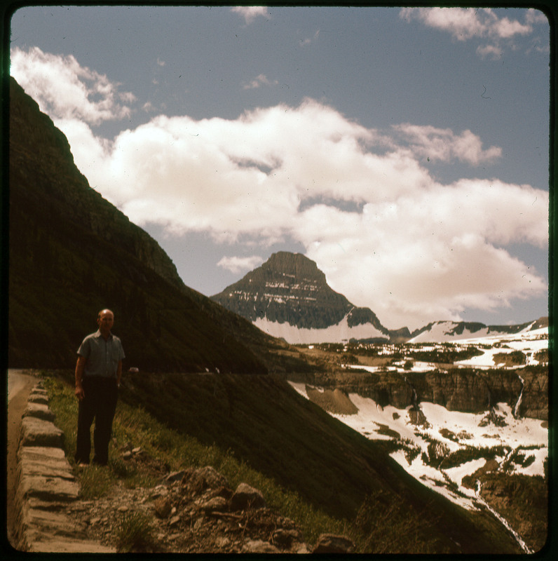 A photographic slide of Donald Crabtree standing in front of a snowy mountain range. Crabtree is hard to see due to the photo being backlit.