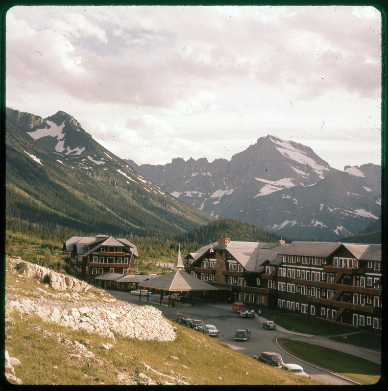 A photographic slide of a snowy mountain range with a large lodge in the foreground. There are cars parked at the lodge.