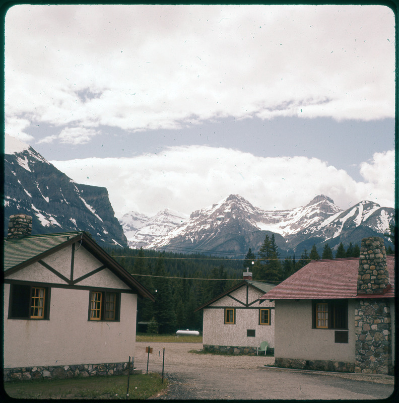 A photographic slide of houses in the foreground and mountains in the background. The mountains are very snowy.