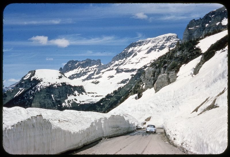 A photographic slide of a snowy mountain range behind an alpine lake. The lake is reflecting the mountain range.