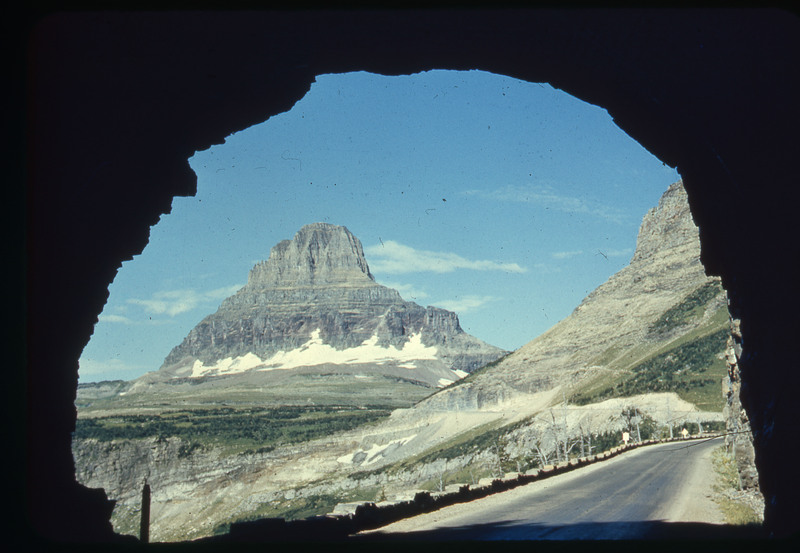 A photographic slide of a sign for Logan Pass. There is a large rocky mountain in the background.