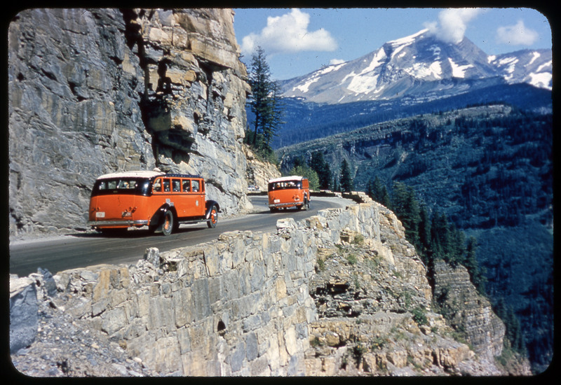 A photographic slide of a standalone rocky mountain with some snow. The photo is taken from a tunnel on a road.