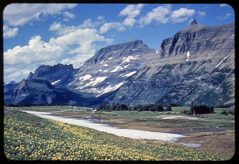 A photographic slide of a mountain range behind a lake. The mountains are reflected in the lake.