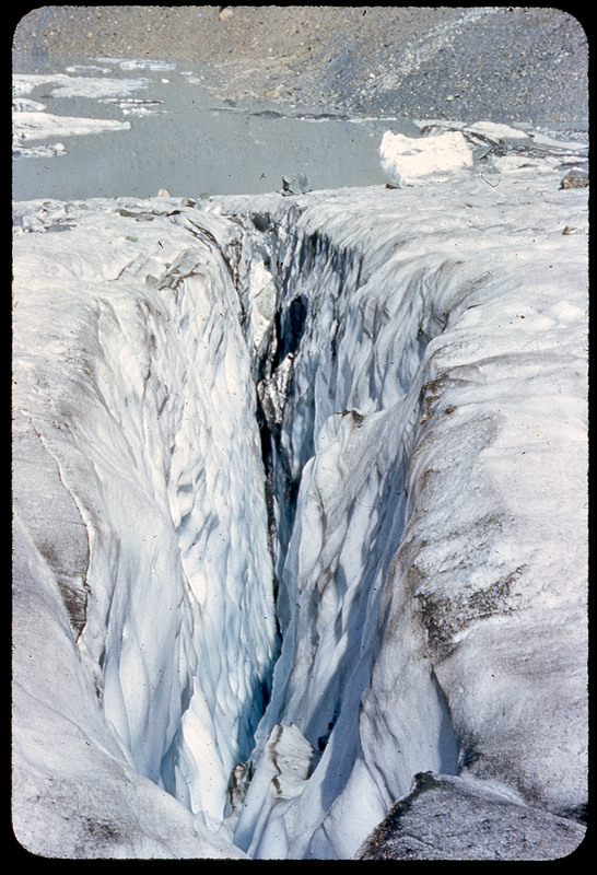 A photographic slide of a glacier crevasse. There is a rocky mountain in the background.