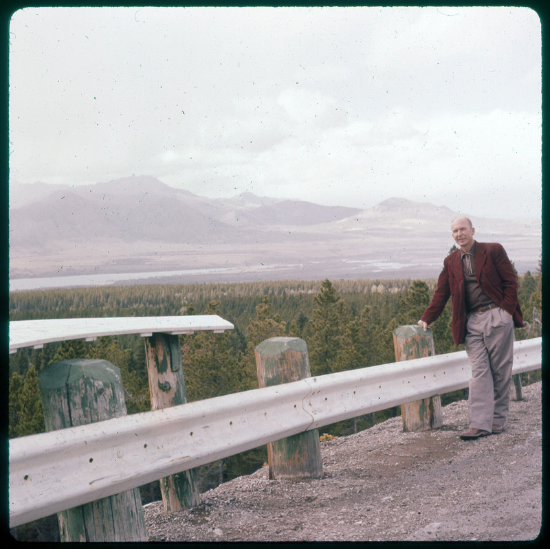 A photographic slide of Donald Crabtree standing in front of a scenic mountain view. There is a field and mountains in the background.