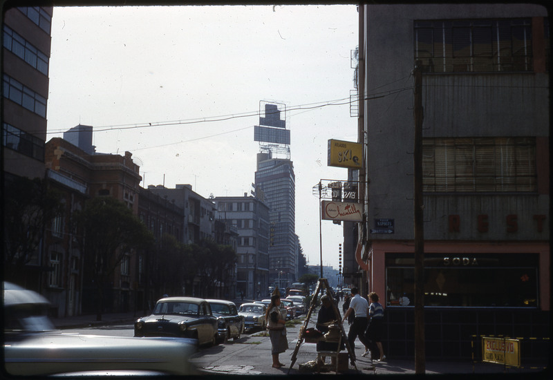 A photographic slide of a busy city road surrounded by tall buildings.