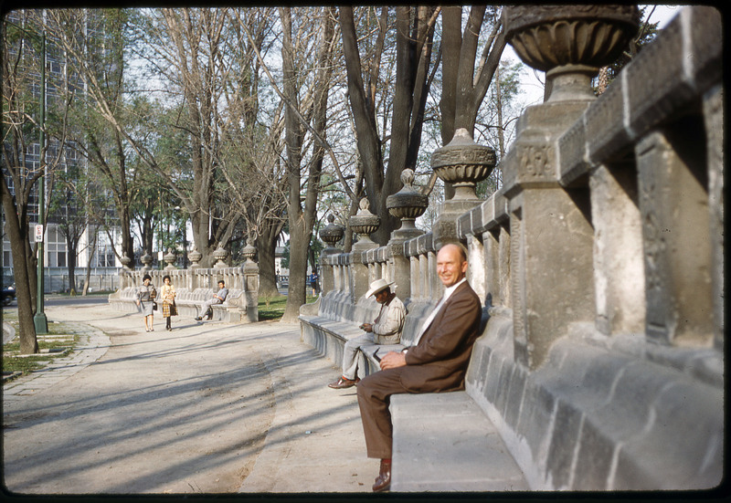 A photographic slide of Don E. Crabtree smiling, sitting on the base of a historical stone wall.