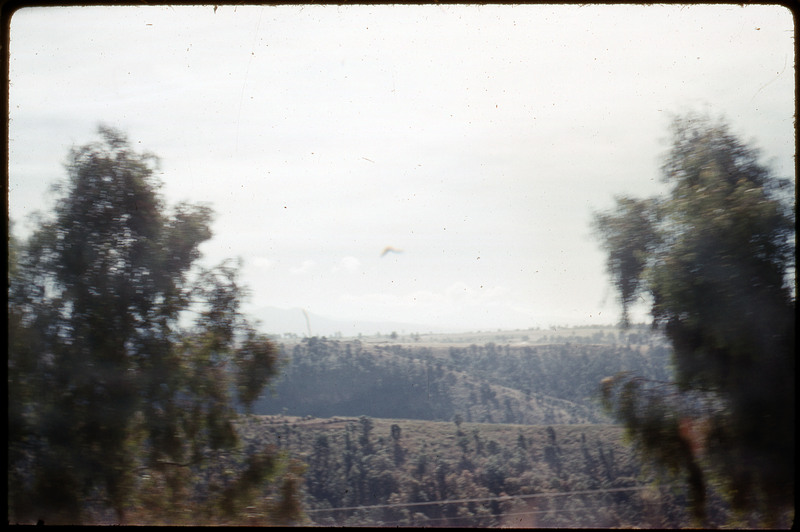 A photographic slide of a valley view. There are hills with many green trees on them.