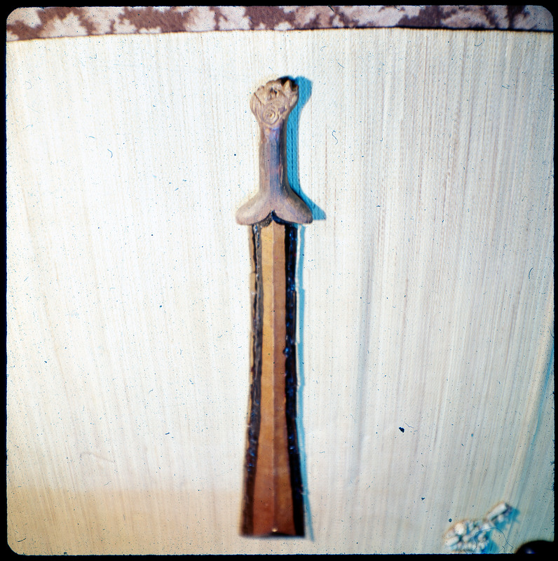 A photographic slide of a structure that resembles a wooden sword. Same as CE_B35_F5-Item20. Has an orange tint.