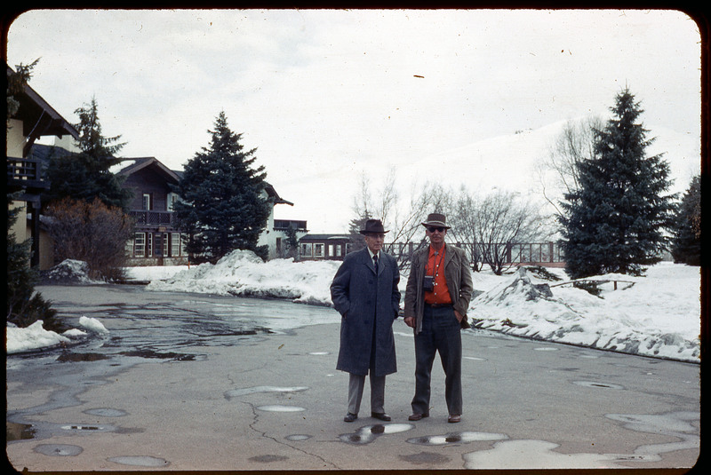 A photographic slide of a man standing next to Donald Crabtree in front of a snowy landscape and house.