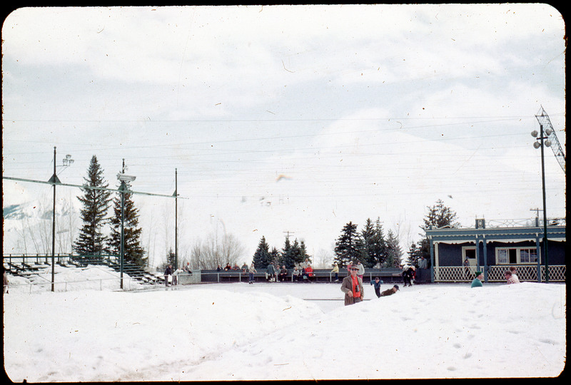 A photographic slide of Donald Crabtree in the snow at an ice skating rink. There are people in the background.