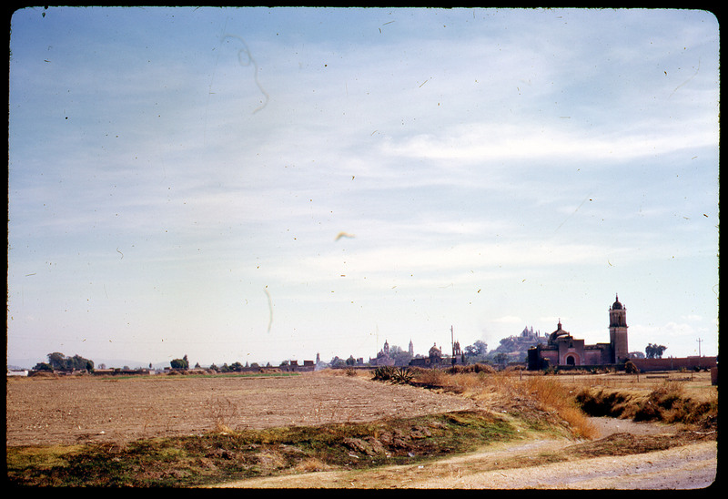 A photographic slide of a cityscape. There is a agricultural field in the foreground and what looks like a church.