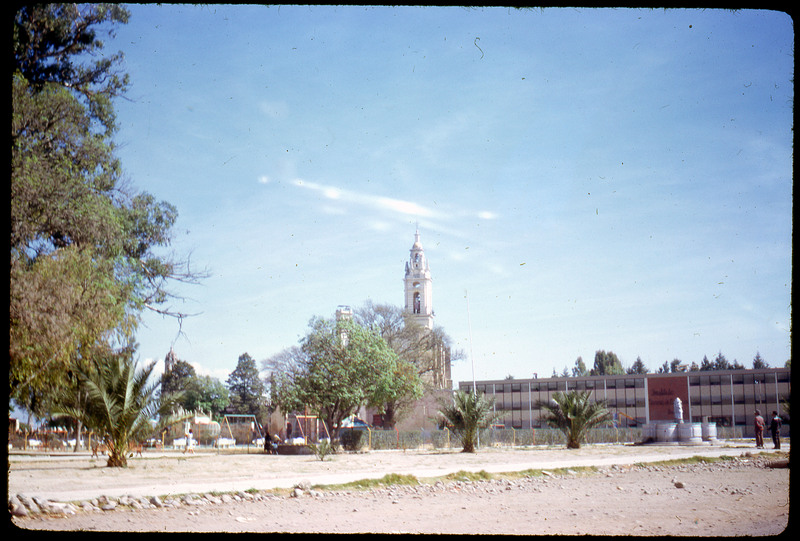 A photographic slide of a large tower in the sky with a park on the ground below it. There are some trees in the front.