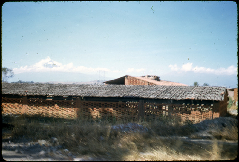 A photographic slide of a structure resembling a barn. There is grass in the foreground and some snow.