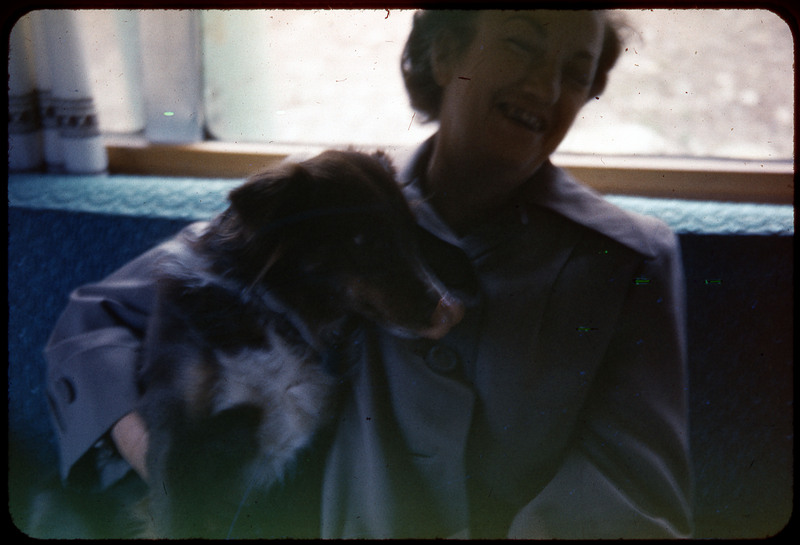 A photographic slide of Evelyn Crabtree with a dog sitting on her lap. She is laughing.