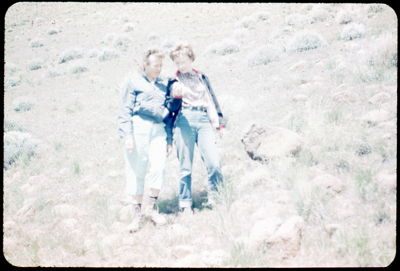 A photographic slide of two people looking at something that one of them is holding. There are standing in a grassy field.