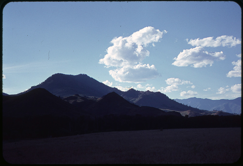 A photographic slide of a mountain range. The sky is blue with clouds.