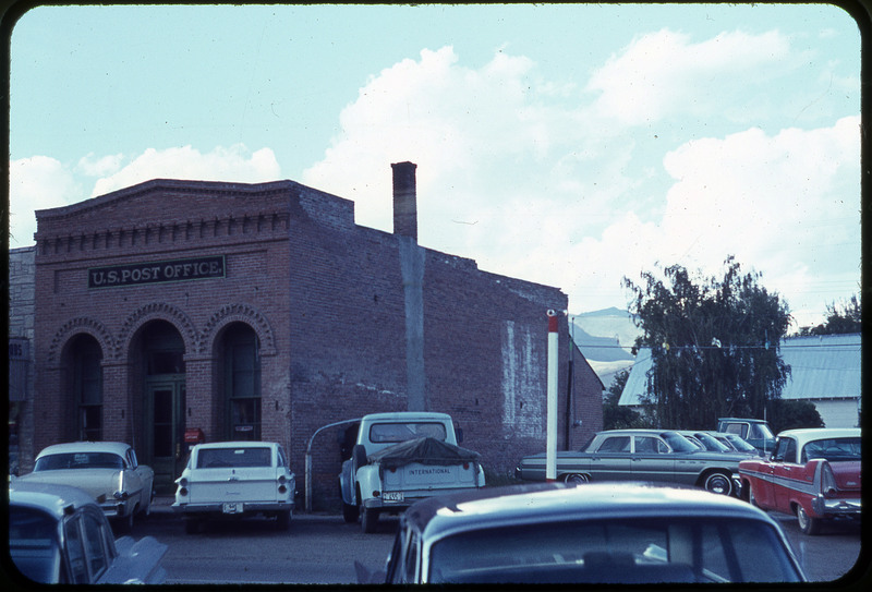 A photographic slide of cars in a parking lot. There is a post office building in the background.