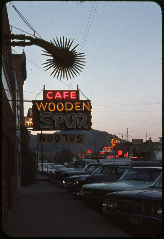 A photographic slide of a sign reading Cafe Wooden. There are cars parked along the sidewalk and it looks to be dusk.