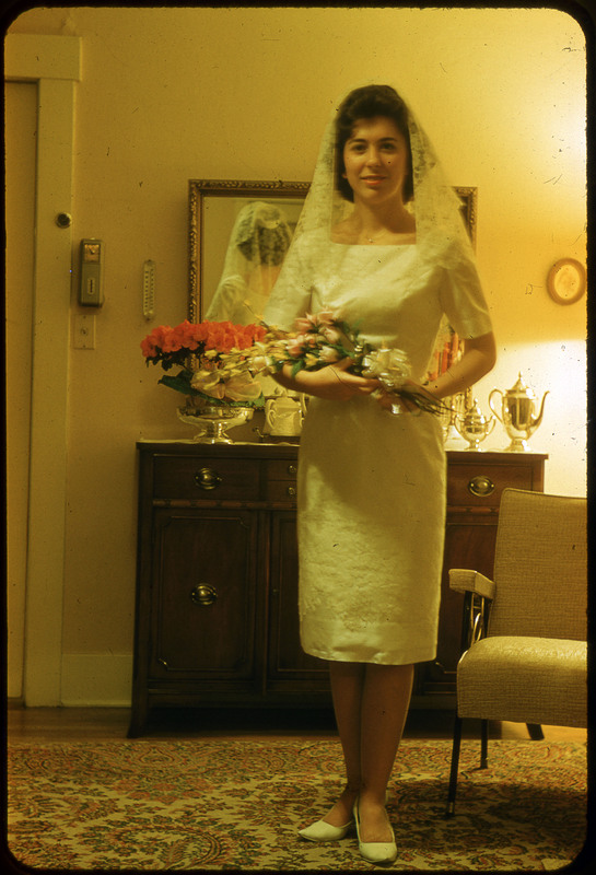 A photographic slide of a woman holding flowers in a wedding dress. She is standing in a nice room and wearing a veil.