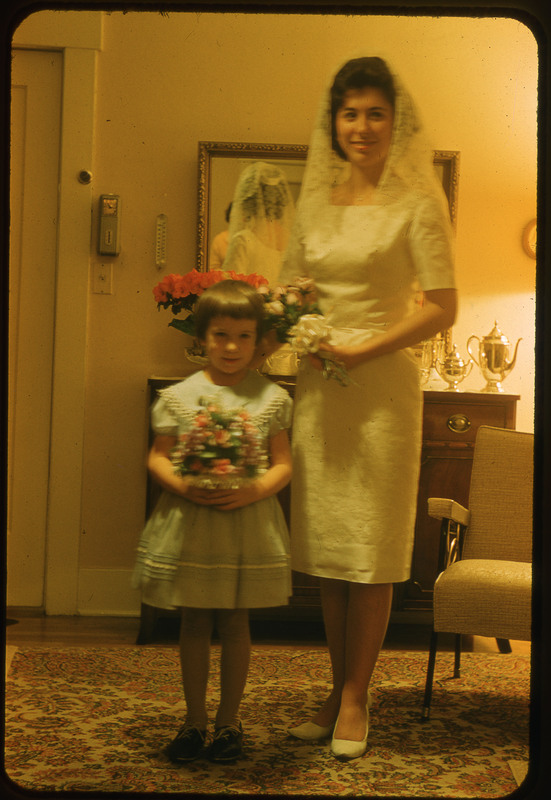 A photographic slide of a woman wearing a wedding dress and holding flowers. She is standing with her arm around a little girl in a dress holding flowers.