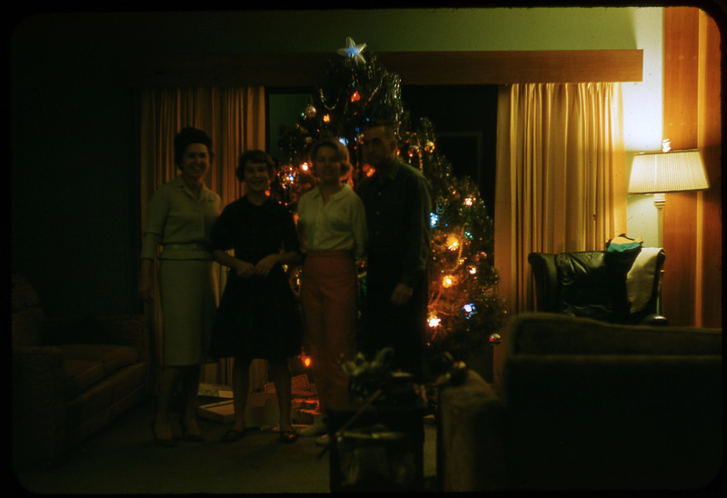 A photographic slide of four people standing in front of a Christmas tree. There are presents under the tree. This could be a family.