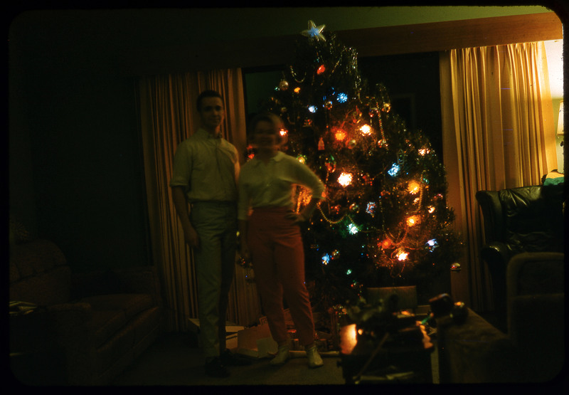 A photographic slide of a couple standing in front of a Christmas tree. There are presents under the tree.