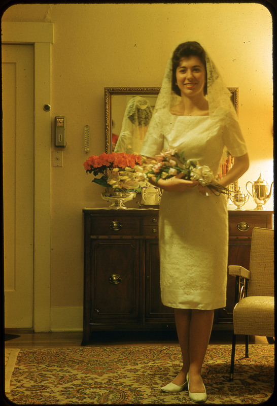 A photographic slide of a person holding flowers in a wedding dress in a nice room.