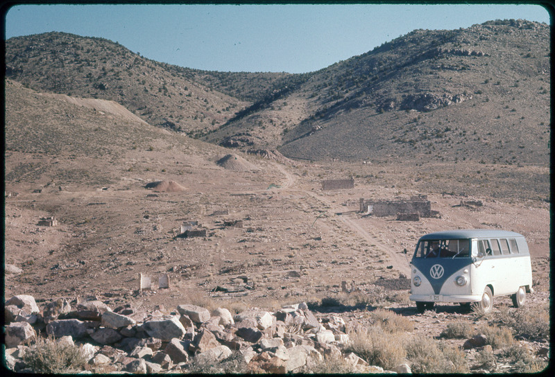 A photographic slide of a VW van parked in a rocky area at the base of some hills.
