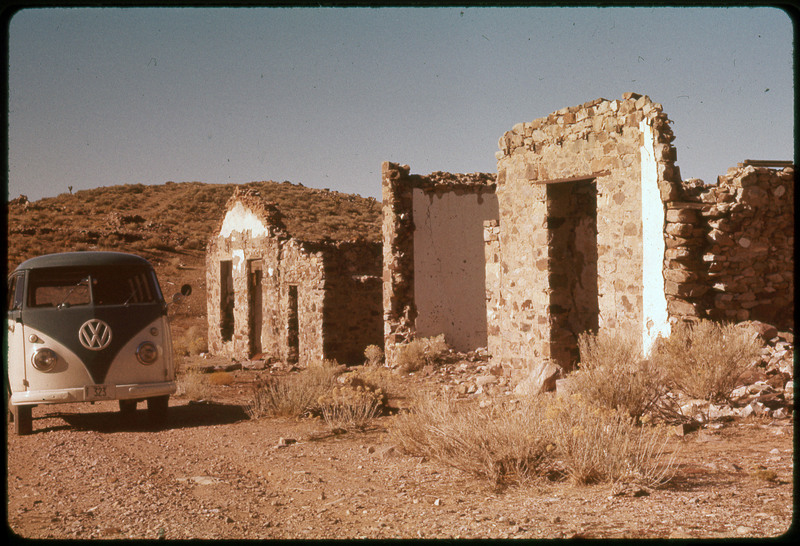 A photographic slide of a VW van parked next to an old brick structure that is falling apart. There is a hill in the background.