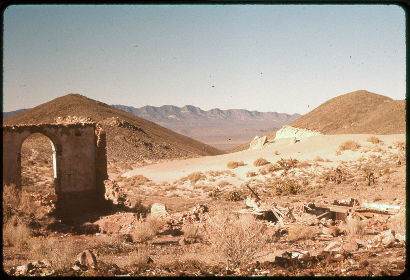 A photographic slide of mountains and an old archway from a previous structure. There is a sand dune.