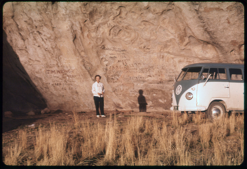 A photographic slide of a giant rock with names written into it. Evelyn Crabtree is assumingly standing in front of the rock with a VW van on the side.