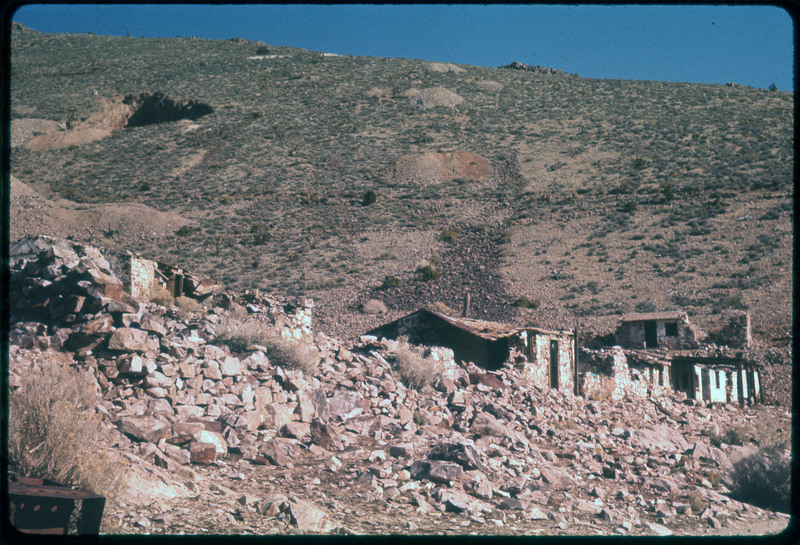 A photographic slide of a rock hillside with old brick buildings built into the base. The structures are falling apart.