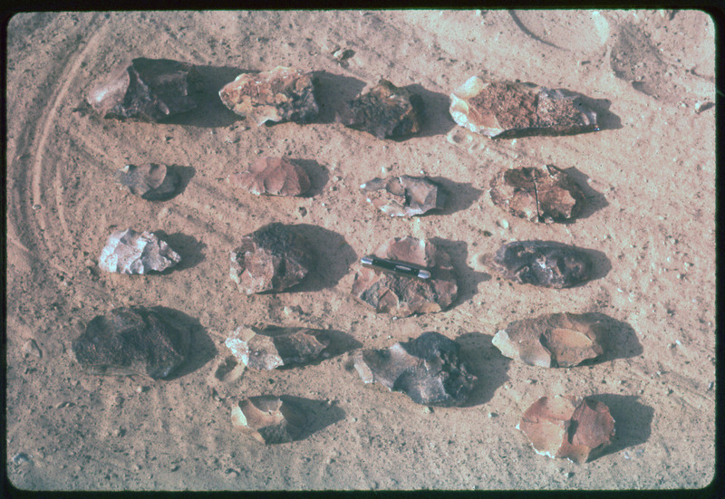 A photographic slide of pieces of flintknapped rock arranged in a grid formation. There is a knife on one in the middle.
