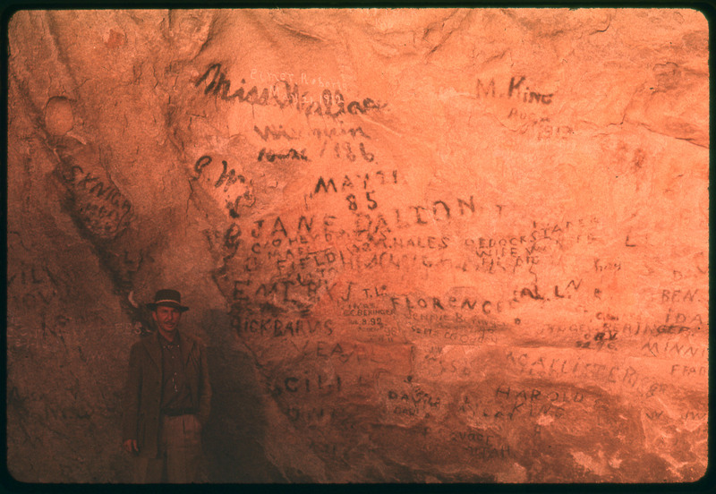 A photographic slide of a rock with names written on it. Donald Crabtree poses in front.